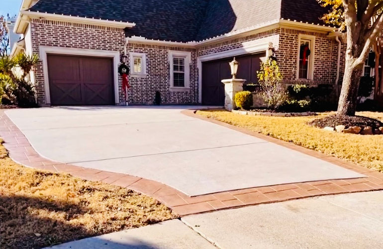 New concrete driveway with a stamped, stained brick-red border leading to a two-car garage at a Dallas brick home