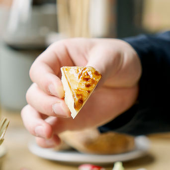 Eine Hand, die ein kleines Stück Käse hält, über das dunkle Glasur geträufelt wurde.