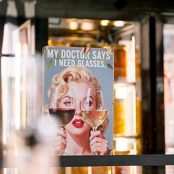 Ein Metallschild mit einer Abbildung von Marilyn Monroe, die zwei Weingläser in der Hand hält, und dem Text: Mein Arzt sagt, ich brauche eine Brille.
