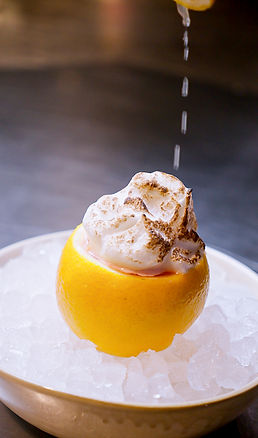 Eine halbierte Grapefruit, gefüllt mit geröstetem Baiser, liegt auf einem Bett aus Eis, während von oben kleine Tropfen auf das Dessert fallen.