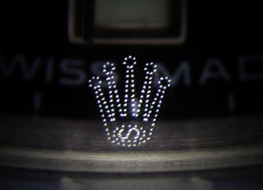 Loupe view of the micro laser‑etched crown on the sapphire crystal.