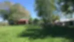 People relax on picnic benches under trees in a sunny farm.