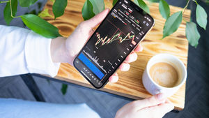 Person sitting, drinking coffee and checking stocks on their phone