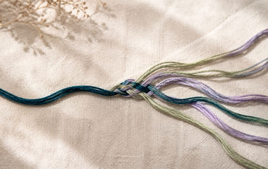 A teal thread intertwined with sage and lavender threads, representing emotional responses becoming connected to an original trigger.