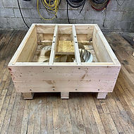 Open wood crate with internal dividers holding metal parts, built on skids