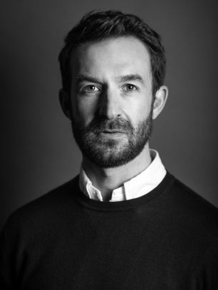 Black and white portrait of Joe Rigby, Northern Managing Director for the north of CBRE in a sweater and collared shirt, with a neutral expression against a plain background.