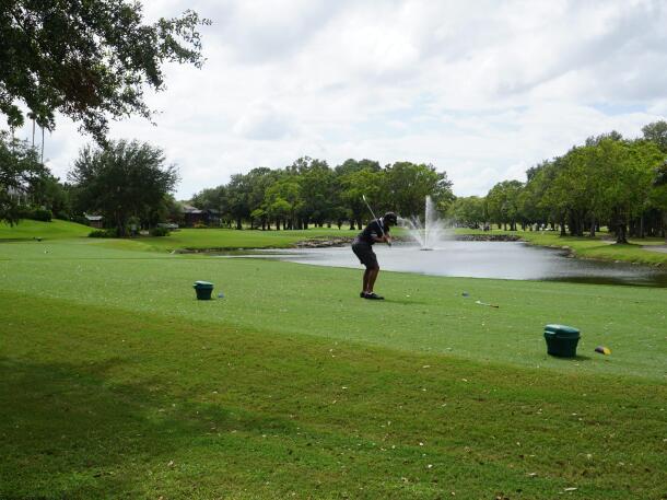 A golfer teeing off beside a fountain pond at Coral Oaks