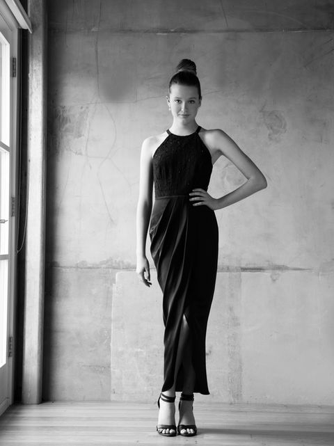 Black and white Musician Photography of a girl with her hair pulled back, wearing a full length black dress, standing in natural light, in front of a concrete wall photo studio backdrop. By Artist Photographer Alise Black Studios