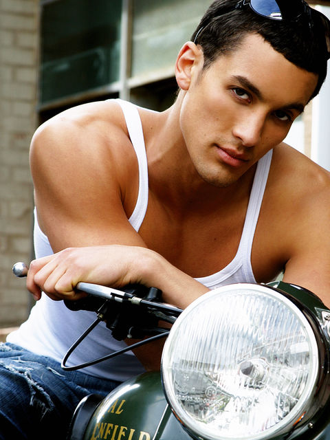 Outdoor Model photoshoot of young man seated on motorbike wearing white tank top and jeans by modelling photographers Alise Black Studios
