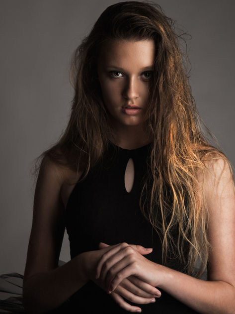 Artist Photography headshot of a girl with wet hair and a serious expression,  standing in front of a dark lit photo studio backdrop, wearing a black dance leotard. Dance Photography by Alise Black Studios