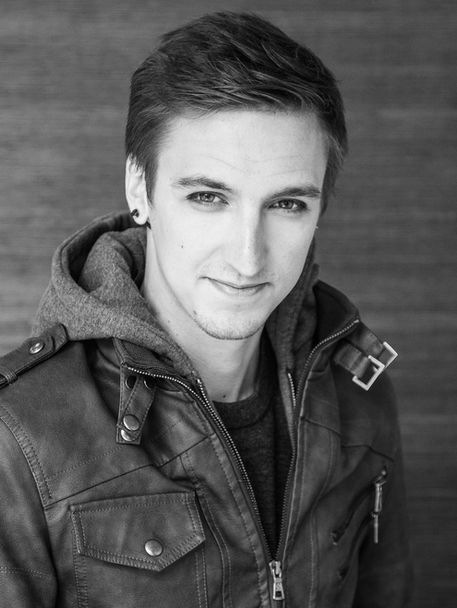 Black and white Portrait of young man with slick hair wearing leather jacket infront of studio backdrop photoshoot by portrait photographer Alise Black Studios