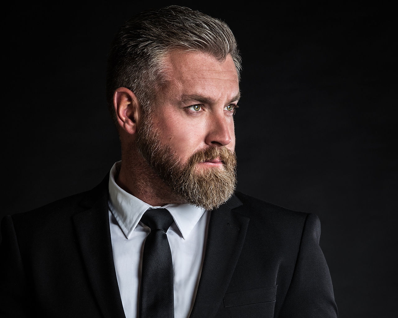 man with beard looking away with black suit and tie by alise black studios