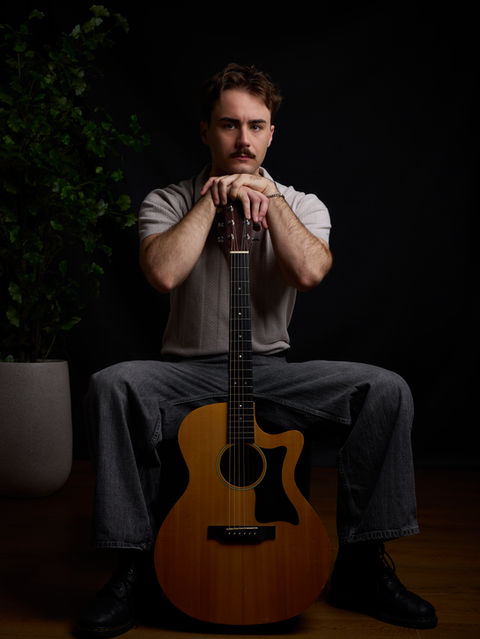 man sitting with guitar with dark background in artist photoshoot by Alise Black Studios