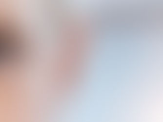 Close-up of a woman’s blue eye and face, softly lit against a blurred pale background, with a calm, attentive expression.