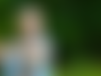 Man in a blue shirt stretches his arm while smiling in a lush green outdoor setting, wearing a black smartwatch.