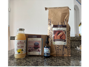 Organic products on a granite counter: lemon juice, frozen blueberries, trace minerals, and coconut sugar in brown packages against a white wall.