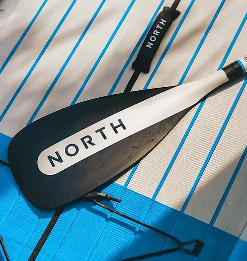 Close-up of North paddleboard and black North paddle with blue striped deck — high-quality