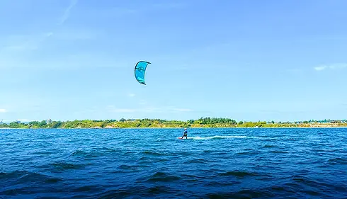 Kiteboarder riding across the ocean with a bright blue kite against clear skies in Victori