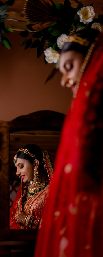 Indian bride is getting ready at Sejal's Beauty Clinic and Academy Surat. Bride is in red outfit, standing in front of a mirror