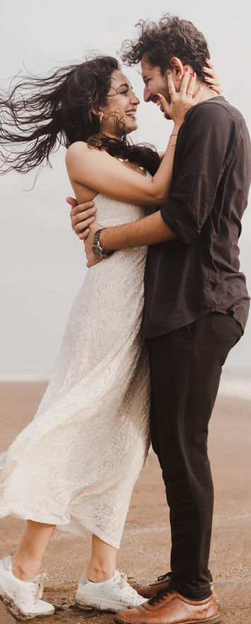 girl is holding his boyfriend's head close to her and laughing candidly while it's raining at a beach