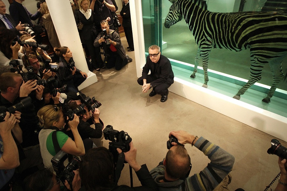 Damien Hirst poses with his work The Incredible Journey at Sotheby’s art gallery and auction house in London on September 8, 2008 Photo by SHAUN CURRY/AFP/Getty Images. Artworks Advisory
