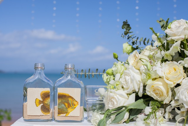 The Ceremony sand created in a fish photo bottle. next to the white flower centerpiece on ceremony flower