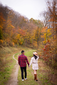 man in red flannel and woman in white flannel walk away from the camera down a tree lined path in the fall