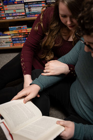 close up of man holding a book open reading it, while woman leans into him