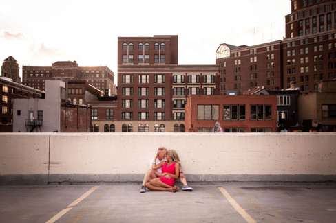 couple sits together in a parking ramp with the City of Buffalo skyline behind them