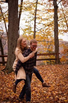man gives woman piggy back ride on foliage filled pathway