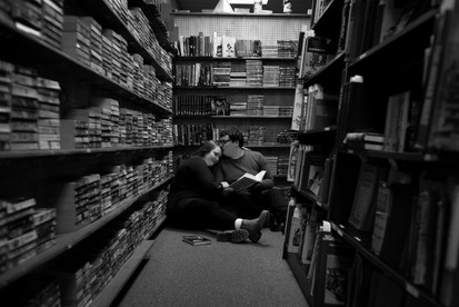 couple sits on the floor of a bookshop cuddled up, he kisses the top of her head