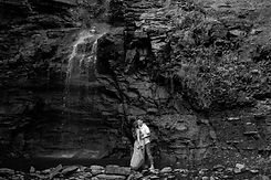 lgbtq couple stands under cliffside waterfall kissing
