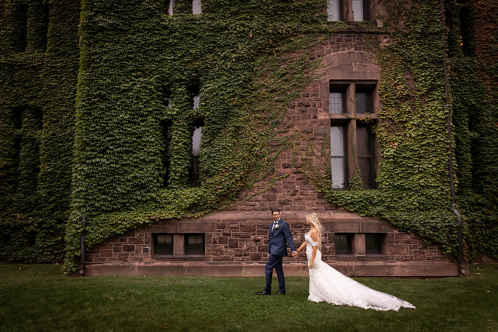 groom leads bride on walk in front of ivy covered stone building