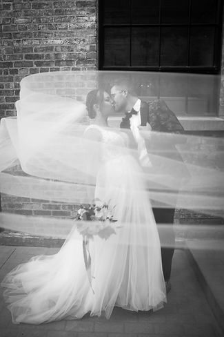 black and white of bride and groom kissing and dipping while the veil flies in front of them