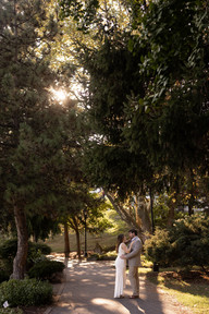couple stands chest to chest on tree lined path with sunlight shining through trees