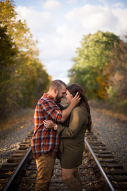 couple stands in the middle of train tracks leaning in forehead to forehead