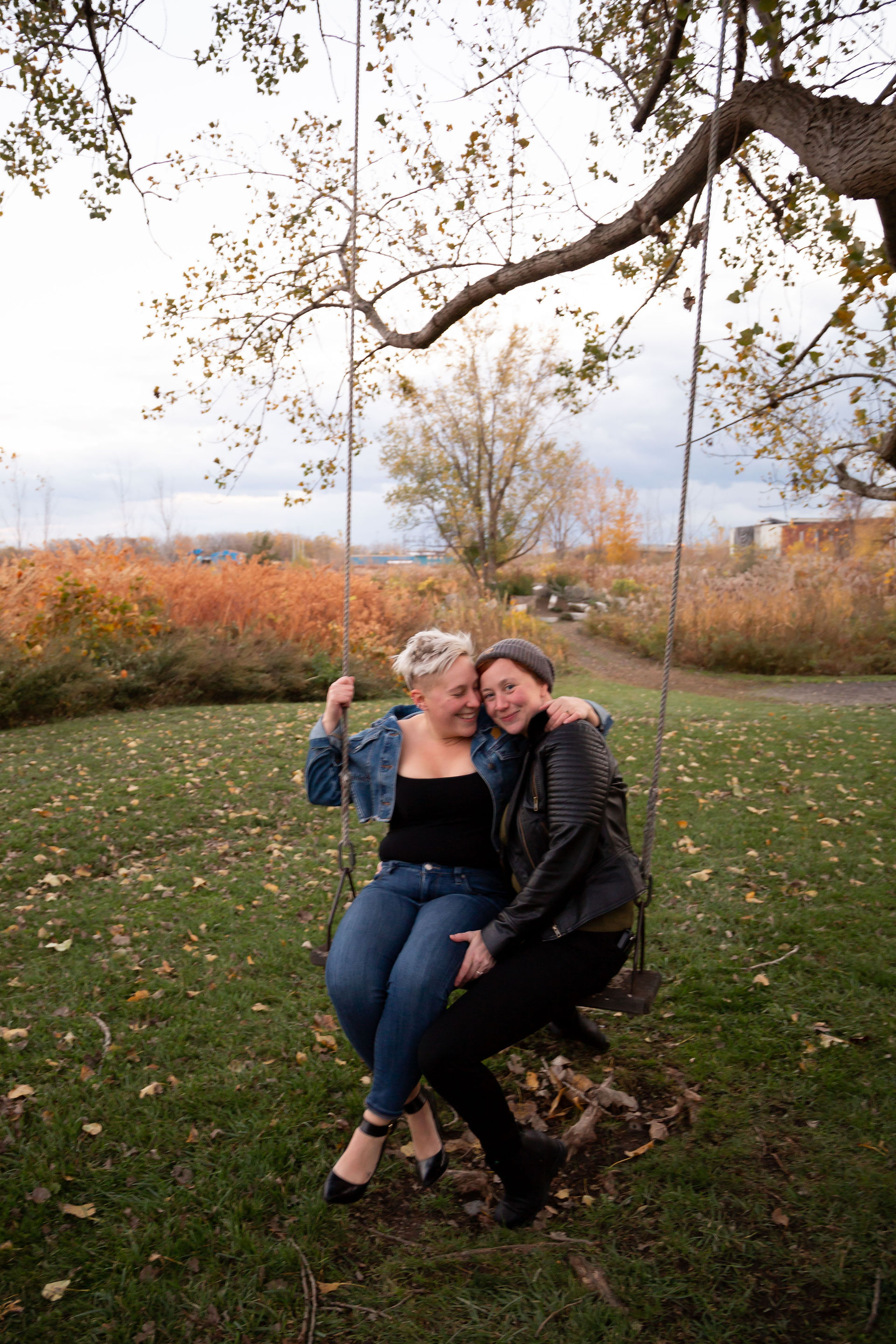 two women sit together on a tree swing leaning into one another
