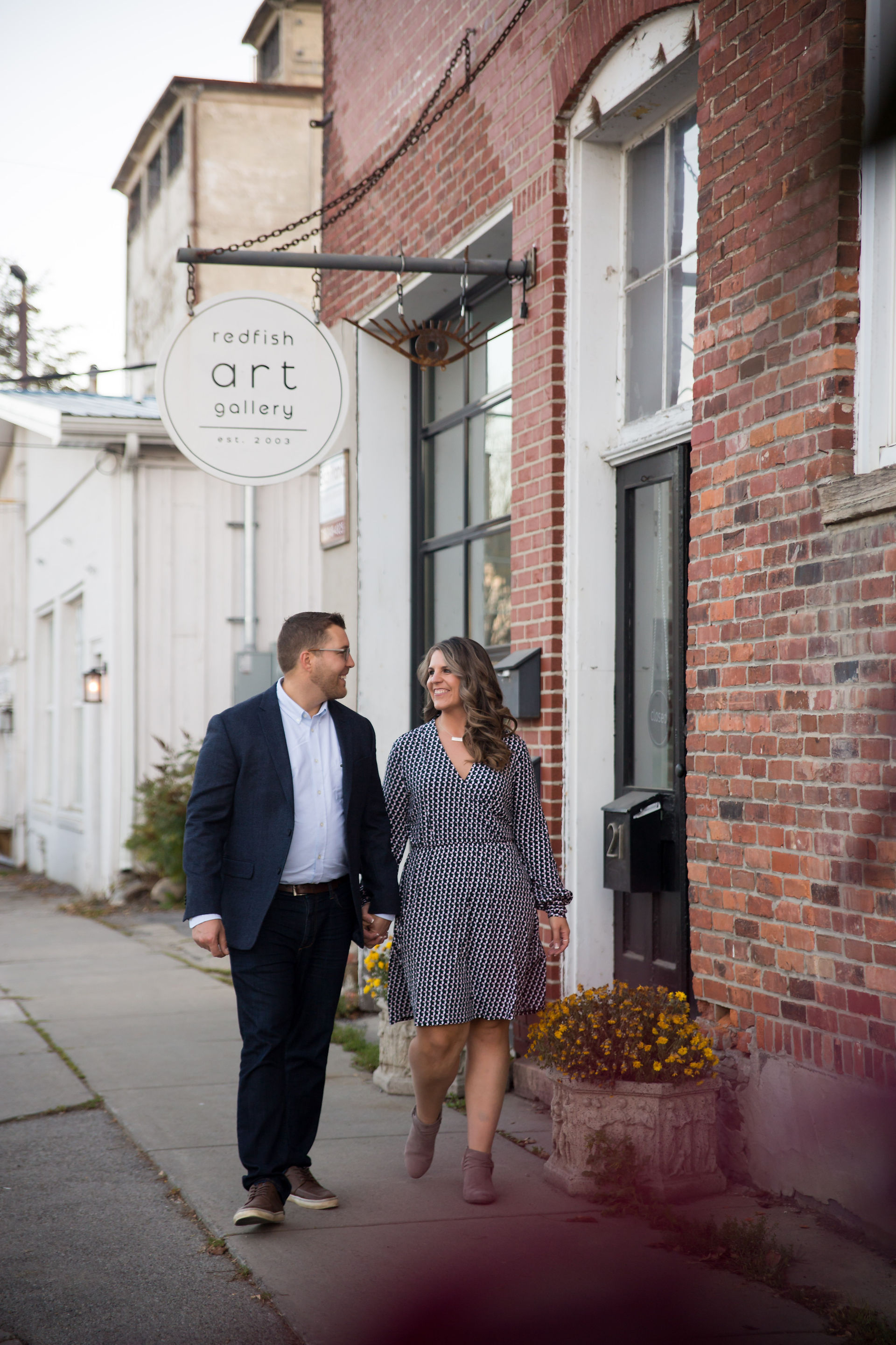 couple walks hand in hand in front of brick building
