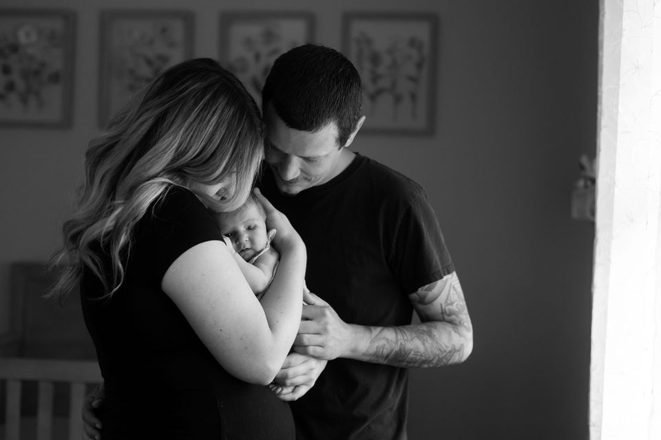 black and white image of mom and dad and newborn baby girl in her nursery