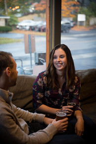 couple sits on a couch in a brewery holding beers and smiling