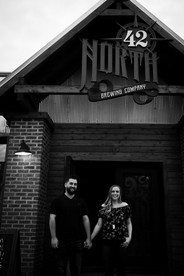 black and white image of couple holding hands in front of 42 North Brewing in East Aurora they're smiling