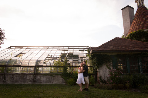 couple stands in front of greenhouse leaning into each other