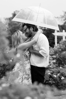 man and woman stand in Delaware Park rose garden about to kiss under a clear bubble umbrella