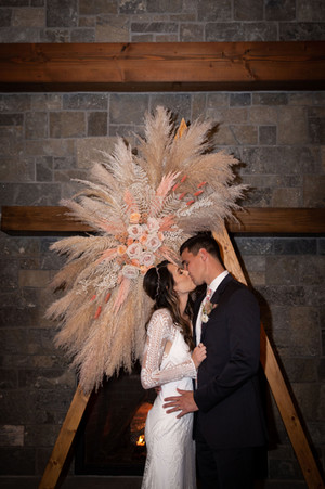 bride and groom kiss at table arch with pampas grass