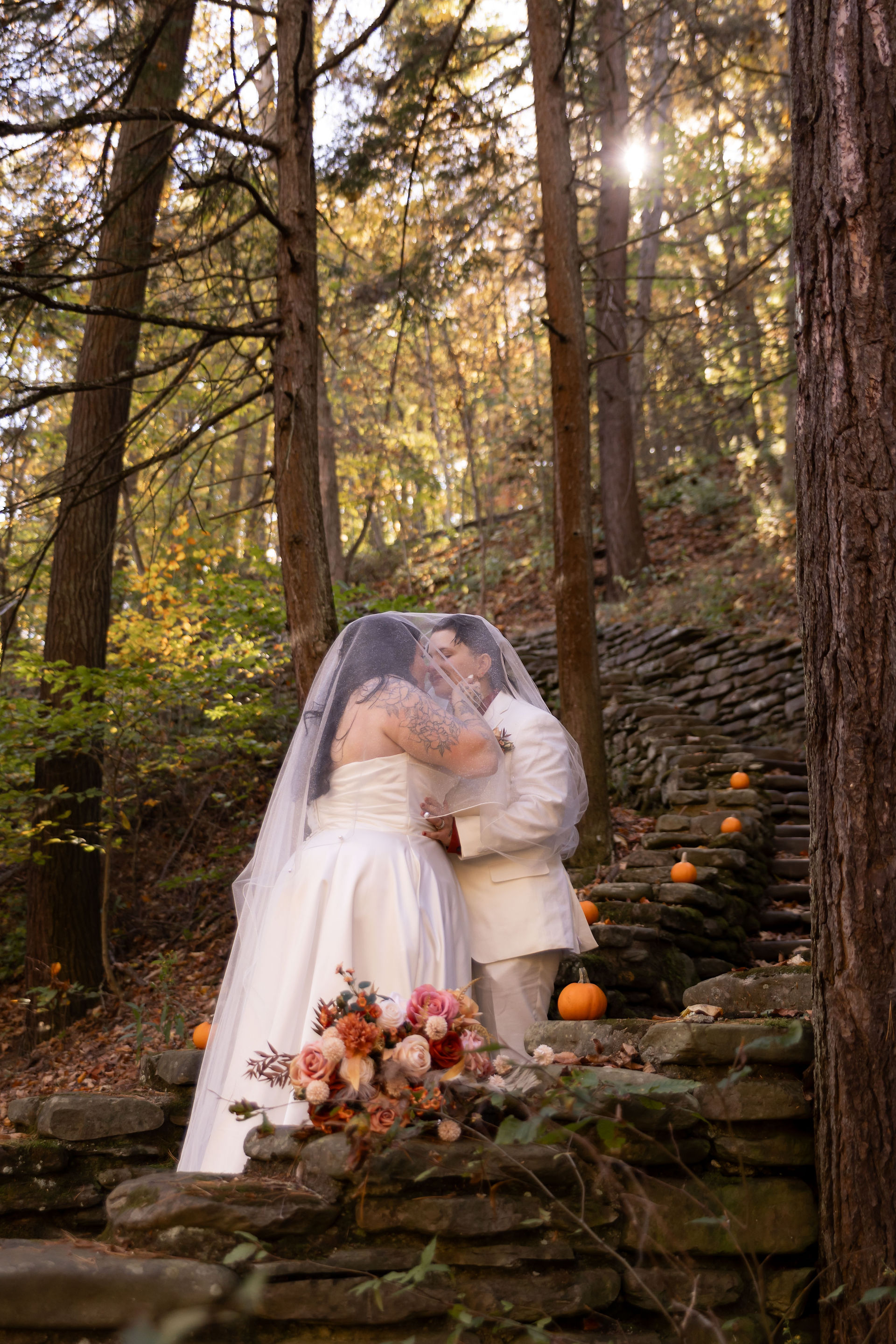 two brides stand kissing under a veil on a stone stair set
