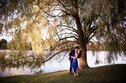 couple does a kiss and dip under a willow tree in front of a lake