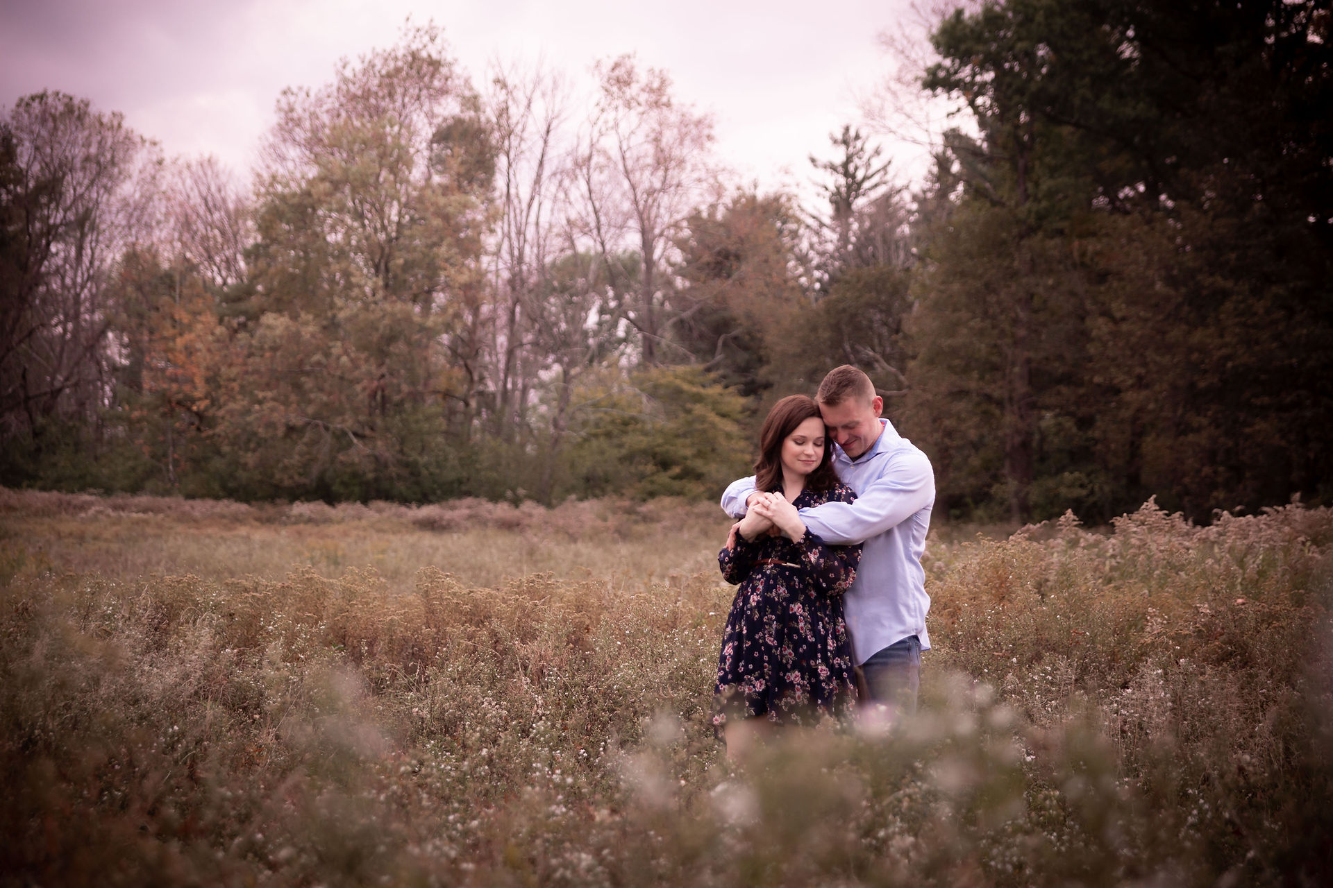 man and woman stand in a field at sunset with a pink sky in background