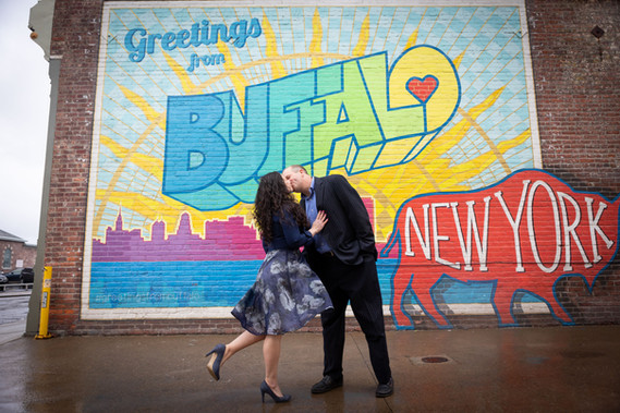 couple kisses in front of greetings from Buffalo postcard mural