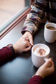close up of a couple's hands holding on a table and coffee mugs