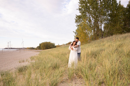 man and woman standing in a field at the edge of a beach leaning into each other